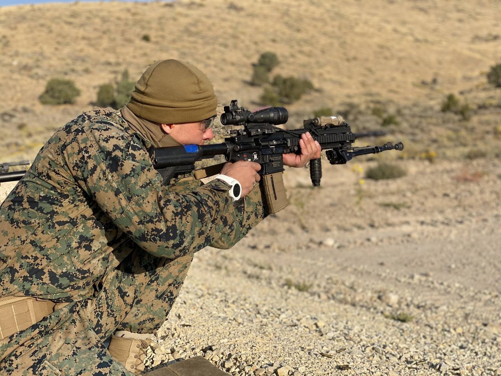 A Marine in a field uniform firing a rifle on a desert range