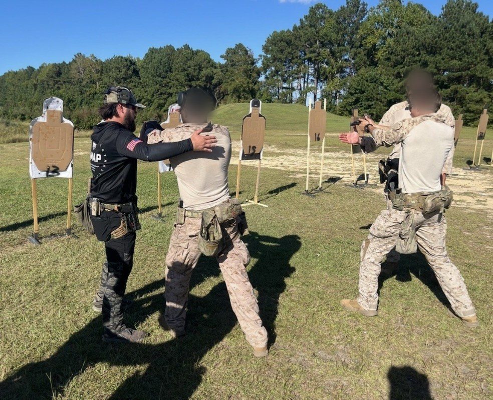 A JMAP instructor hands-on coaching a service member at the targets; faces blurred
